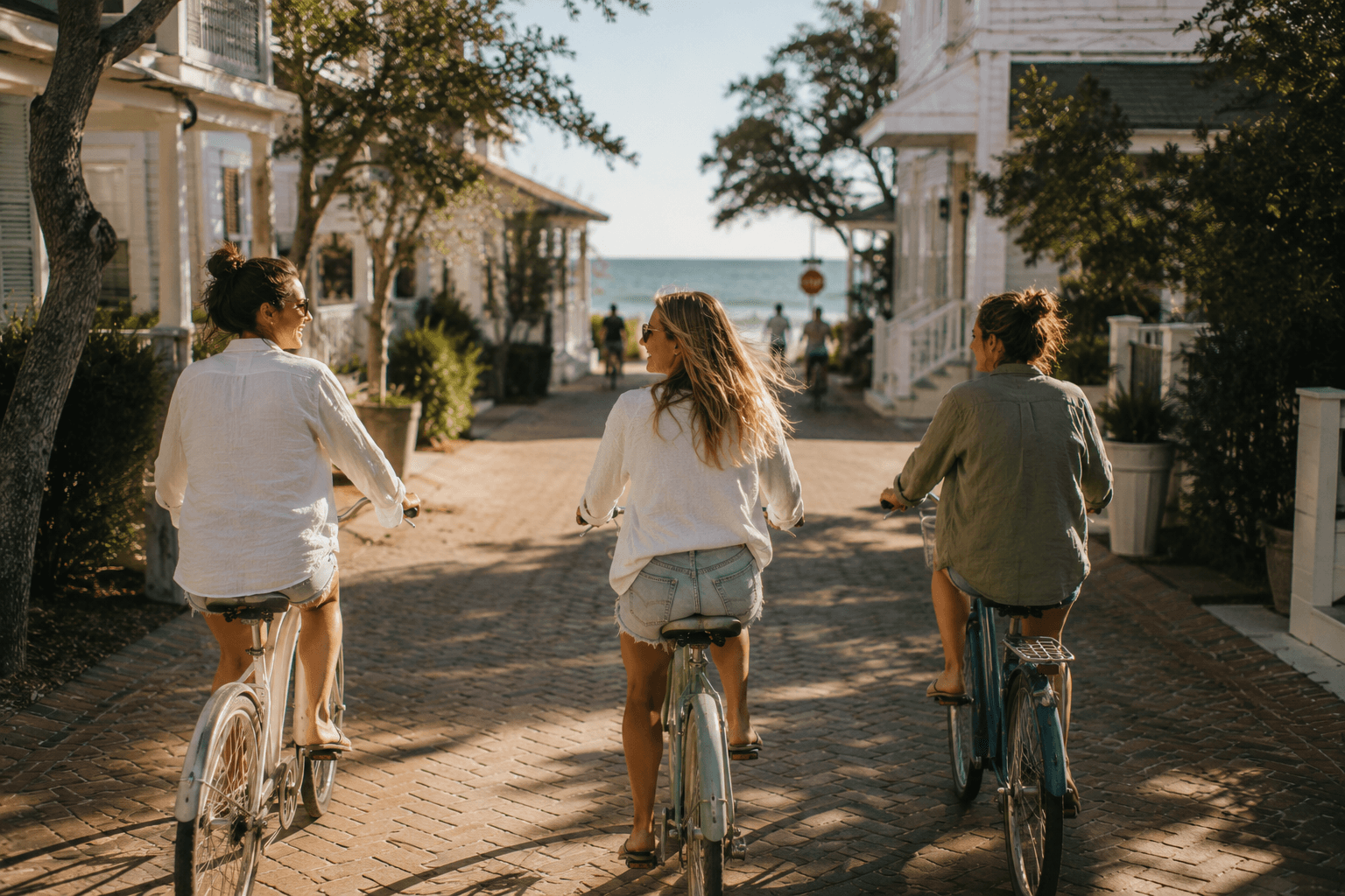 Three friends riding bicycles through a sunny coastal town toward the beach.